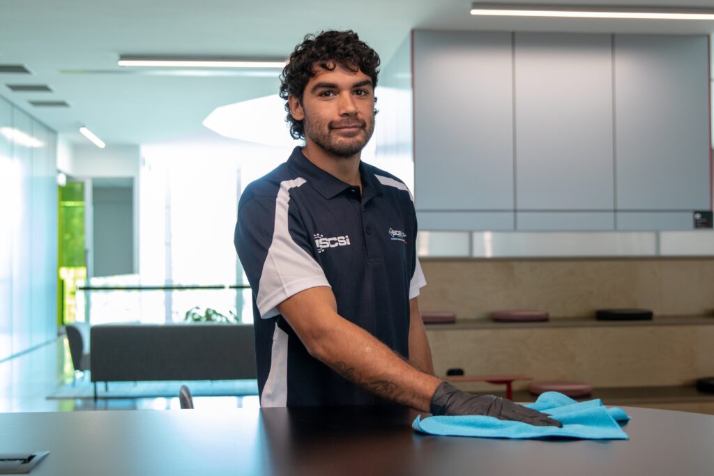 Professional commercial cleaner wiping a reception counter with a microfibre cloth in a modern office environment, demonstrating high quality workplace cleaning and surface sanitisation.
