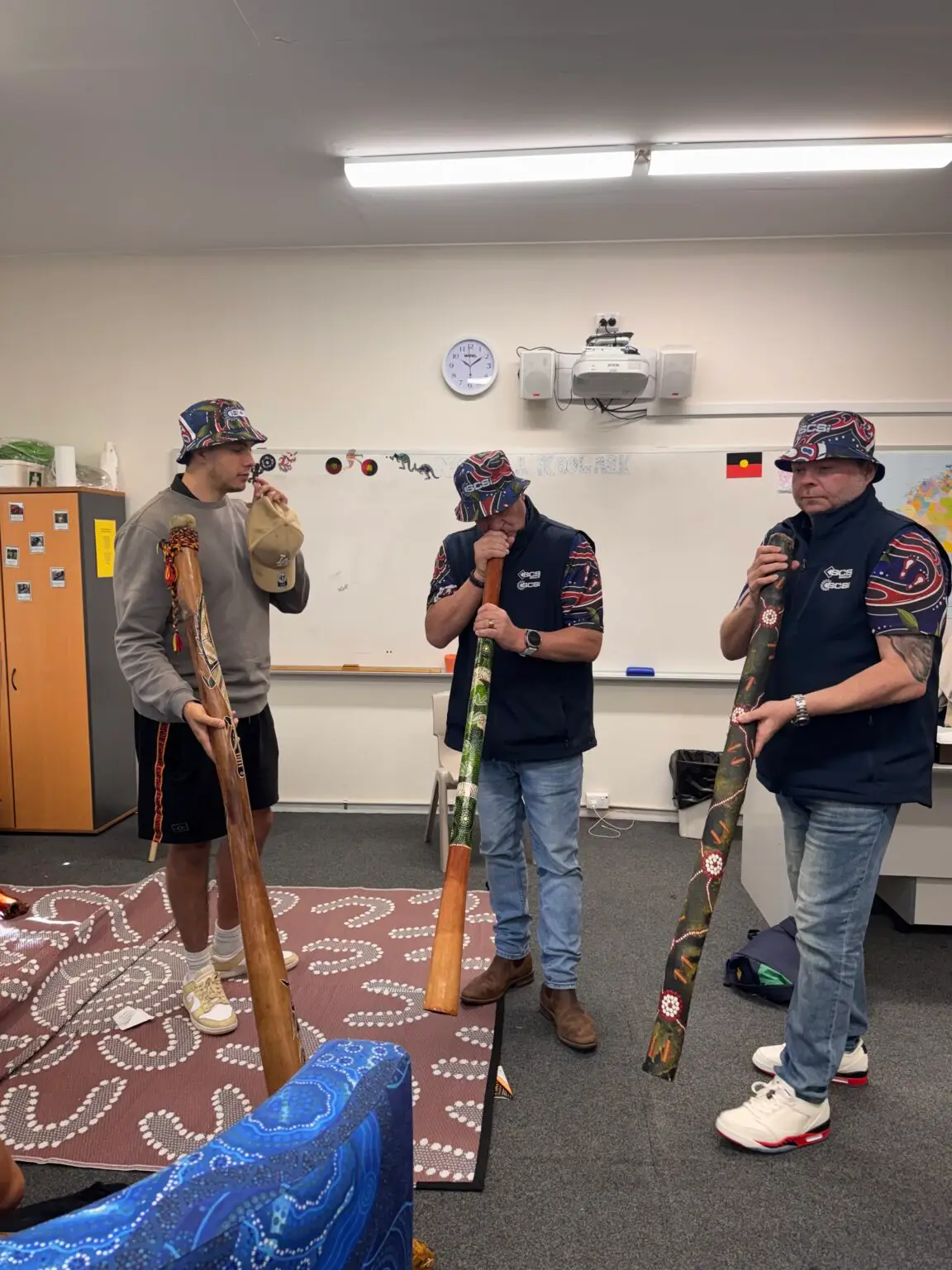 Tryse, Nick, and Scott trying out the didgeridoos during their school site visit.